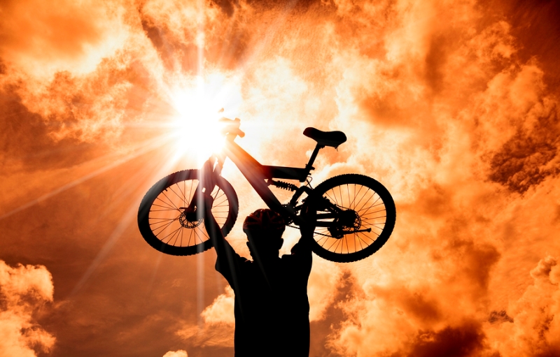 The Silhouette of muontain biker raised bicycle with sunset and cloud background